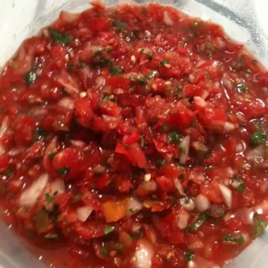 Close-up of fresh homemade salsa with tomatoes, onions, jalapeños, and cilantro in a clear container
