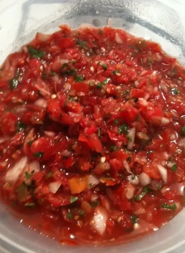 Close-up of fresh homemade salsa with tomatoes, onions, jalapeños, and cilantro in a clear container