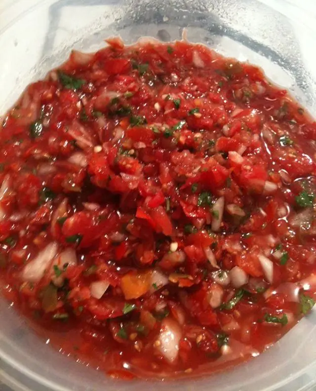 Close-up of fresh homemade salsa with tomatoes, onions, jalapeños, and cilantro in a clear container