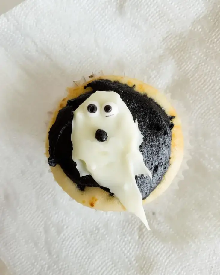Halloween ghost cupcake with fluffy white frosting shaped like a ghost and candy eyes on dark chocolate icing base