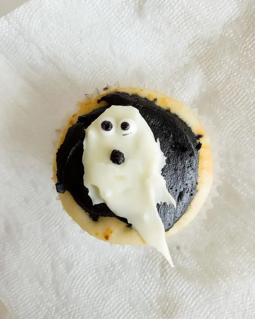 Halloween ghost cupcake with fluffy white frosting shaped like a ghost and candy eyes on dark chocolate icing base