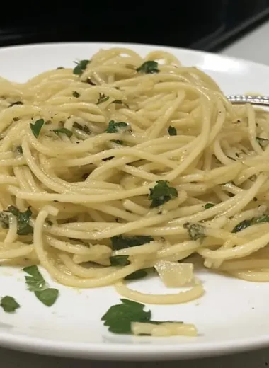 Plated spaghetti aglio e olio with golden olive oil coating pasta strands, fresh parsley garnish, and fork on white dinner plate