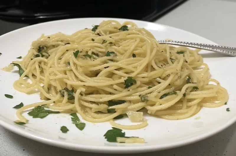 Plated spaghetti aglio e olio with golden olive oil coating pasta strands, fresh parsley garnish, and fork on white dinner plate