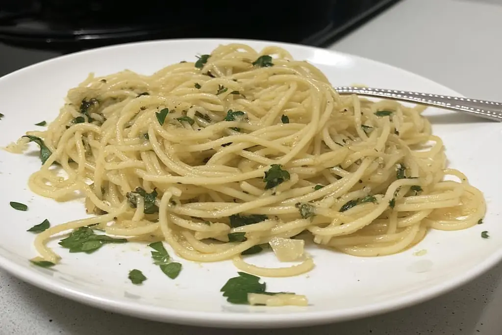Plated spaghetti aglio e olio with golden olive oil coating pasta strands, fresh parsley garnish, and fork on white dinner plate