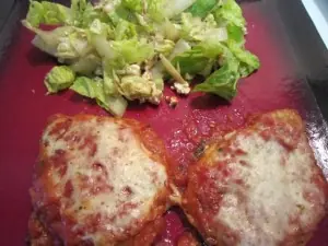 Baked chicken Parmesan topped with melted mozzarella and marinara, served with a chopped romaine salad on a red plate.