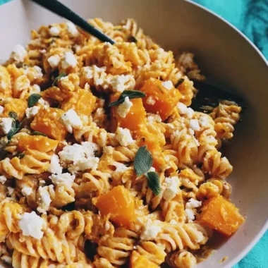 Bowl of rotini coated in creamy butternut squash sauce with roasted squash cubes, crumbled feta, and fresh sage leaves.