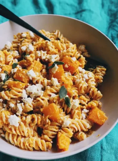 Bowl of rotini coated in creamy butternut squash sauce with roasted squash cubes, crumbled feta, and fresh sage leaves.