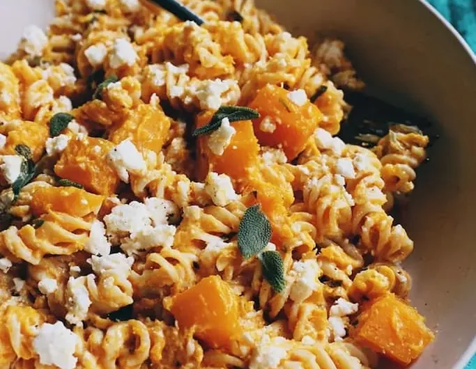 Bowl of rotini coated in creamy butternut squash sauce with roasted squash cubes, crumbled feta, and fresh sage leaves.