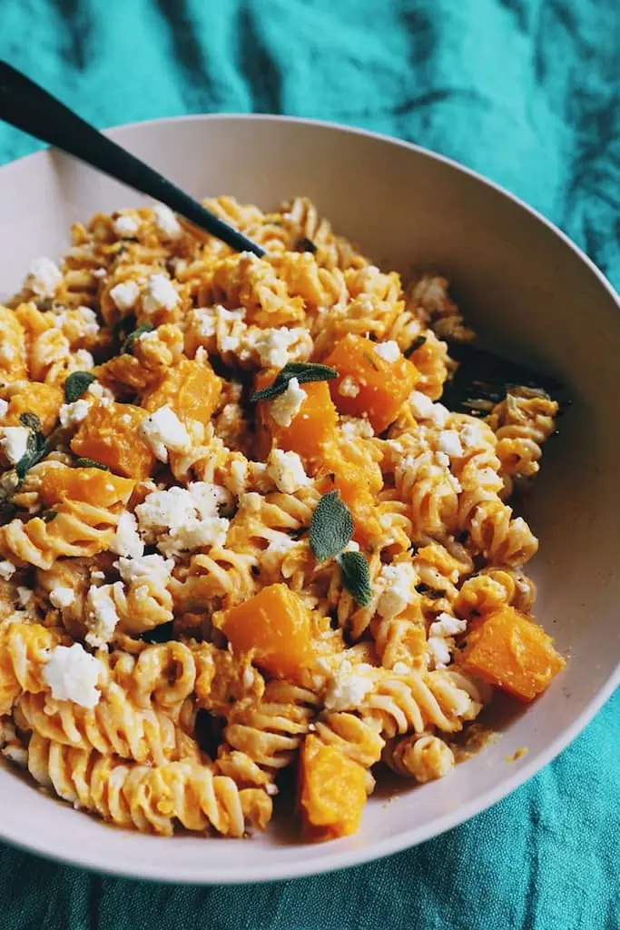 Bowl of rotini coated in creamy butternut squash sauce with roasted squash cubes, crumbled feta, and fresh sage leaves.
