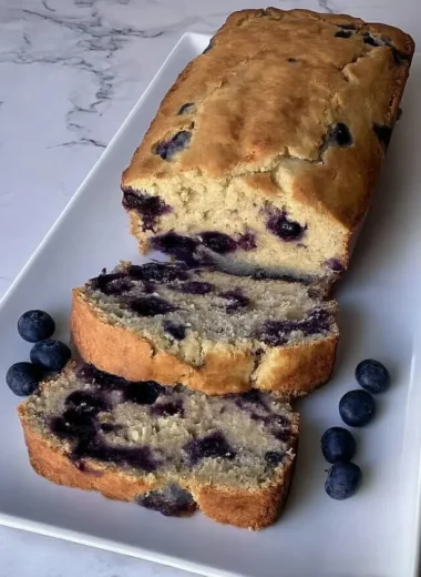 Golden brown blueberry cottage cheese breakfast cake loaf with two slices cut showing moist interior packed with fresh blueberries on white serving plate