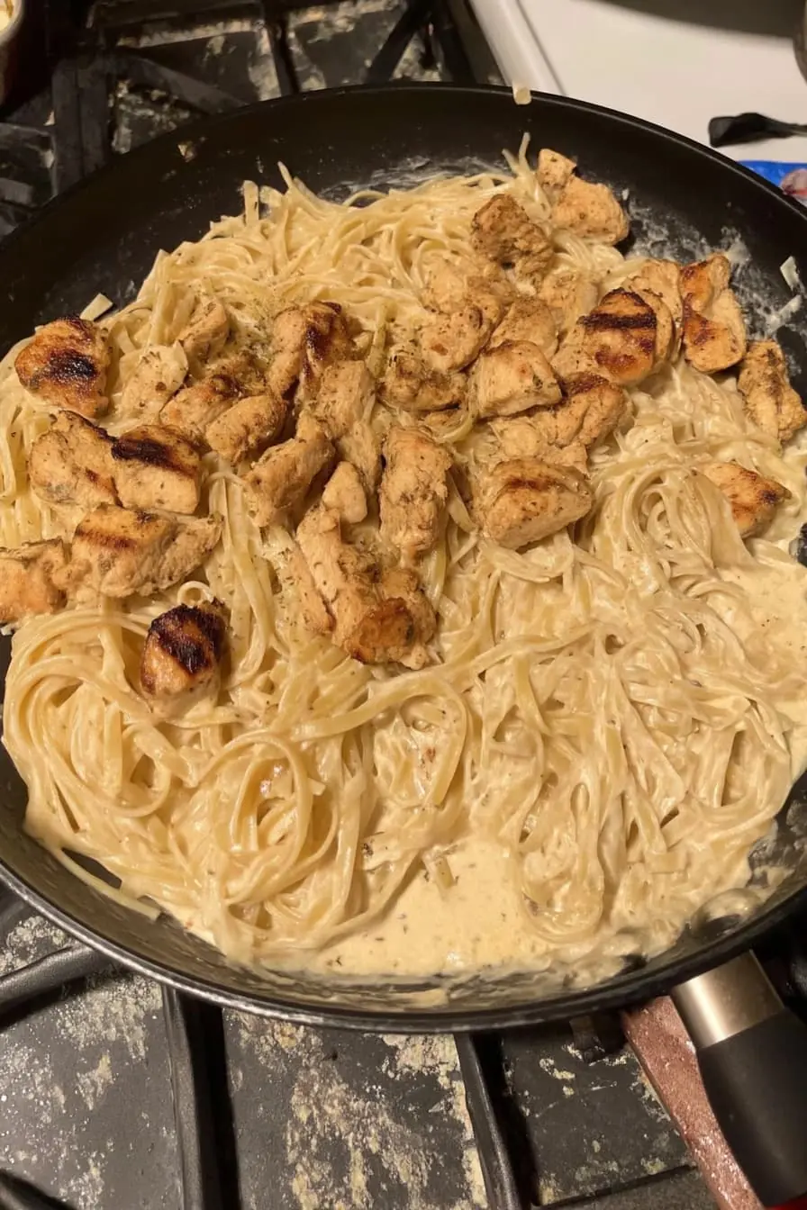Creamy butter garlic chicken pasta in a non-stick skillet, topped with browned grilled chicken pieces.