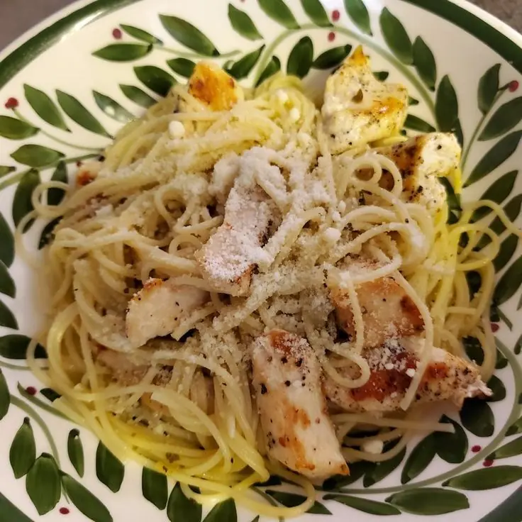 Close-up of butter garlic sauce grilled chicken over angel-hair pasta, sprinkled with grated Parmesan in a patterned bowl.