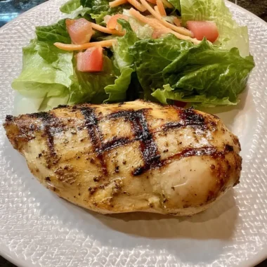 Juicy Cajun-spiced grilled chicken breast with crisp romaine, tomato, and carrot salad on a textured white plate.
