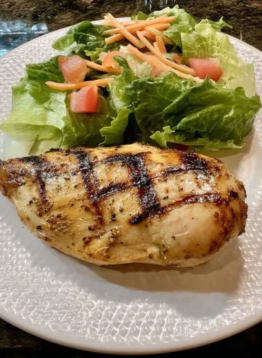 Juicy Cajun-spiced grilled chicken breast with crisp romaine, tomato, and carrot salad on a textured white plate.
