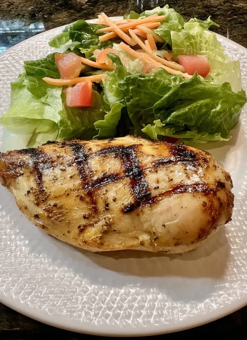 Juicy Cajun-spiced grilled chicken breast with crisp romaine, tomato, and carrot salad on a textured white plate.