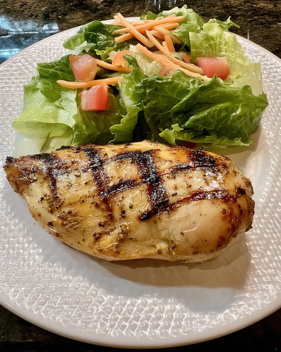 Juicy Cajun-spiced grilled chicken breast with crisp romaine, tomato, and carrot salad on a textured white plate.