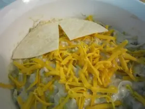 Layering corn tortillas and shredded cheddar over creamy chicken enchilada casserole