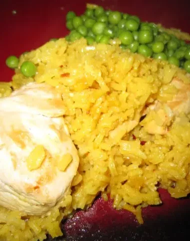 Close-up of homemade Arroz Con Pollo with yellow rice, tender chicken pieces, and a side of green peas on a red plate