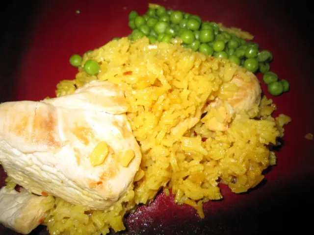 Close-up of homemade Arroz Con Pollo with yellow rice, tender chicken pieces, and a side of green peas on a red plate