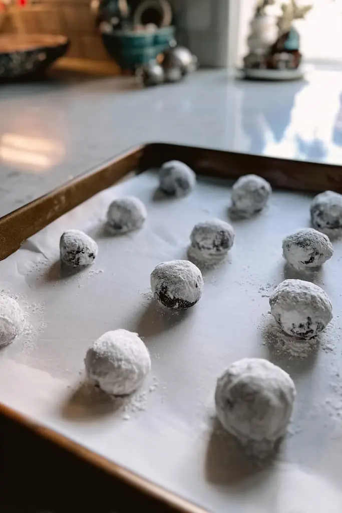 Chocolate cookie dough balls generously coated in powdered sugar on parchment-lined baking sheet ready to bake