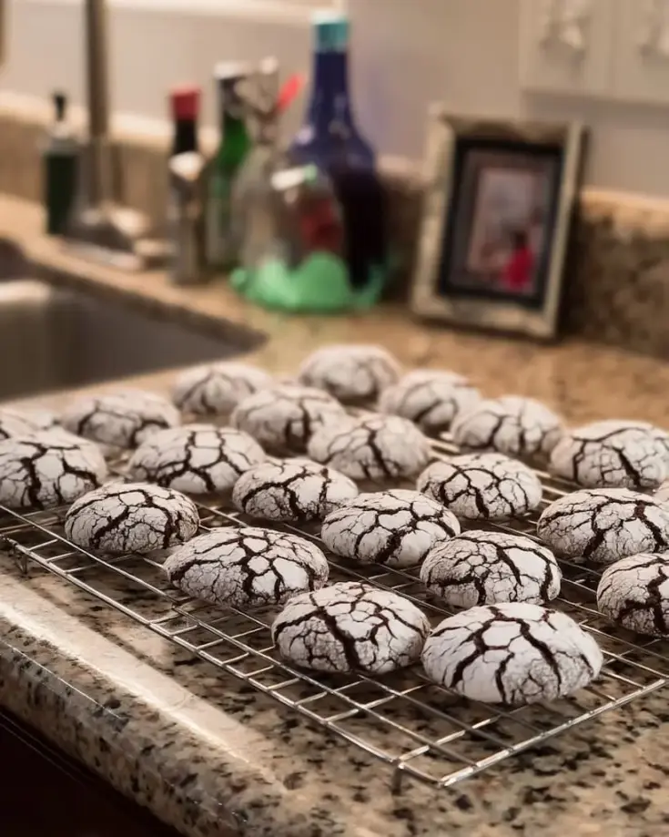 Freshly baked chocolate crinkle cookies with dramatic powdered sugar cracks cooling on wire rack