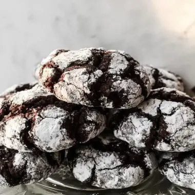 Stack of chocolate crinkle cookies with dramatic powdered sugar cracks on clear glass plate