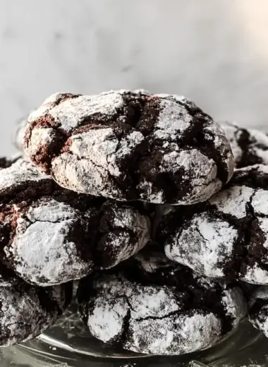 Stack of chocolate crinkle cookies with dramatic powdered sugar cracks on clear glass plate