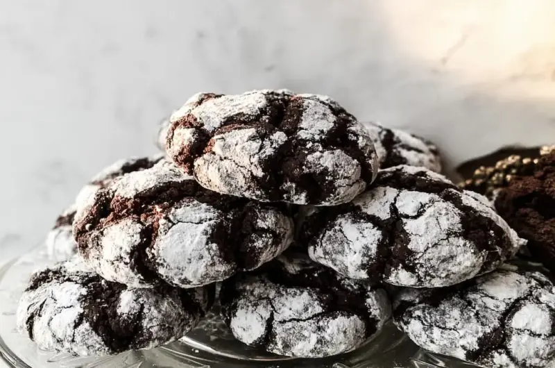 Stack of chocolate crinkle cookies with dramatic powdered sugar cracks on clear glass plate