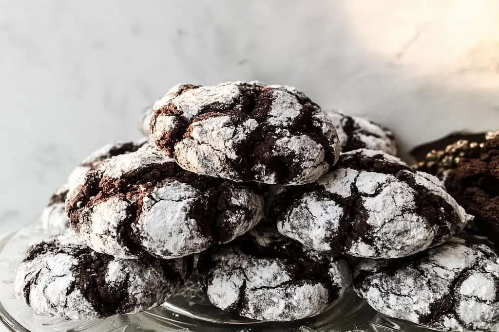 Stack of chocolate crinkle cookies with dramatic powdered sugar cracks on clear glass plate