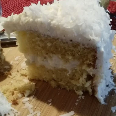 A thick, fluffy slice of homemade coconut cloud cake with three layers of moist yellow cake and creamy coconut frosting, topped with shredded coconut.