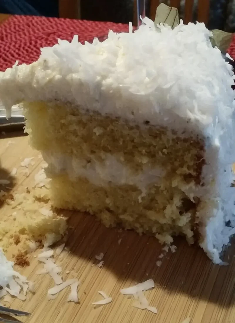 A thick, fluffy slice of homemade coconut cloud cake with three layers of moist yellow cake and creamy coconut frosting, topped with shredded coconut.