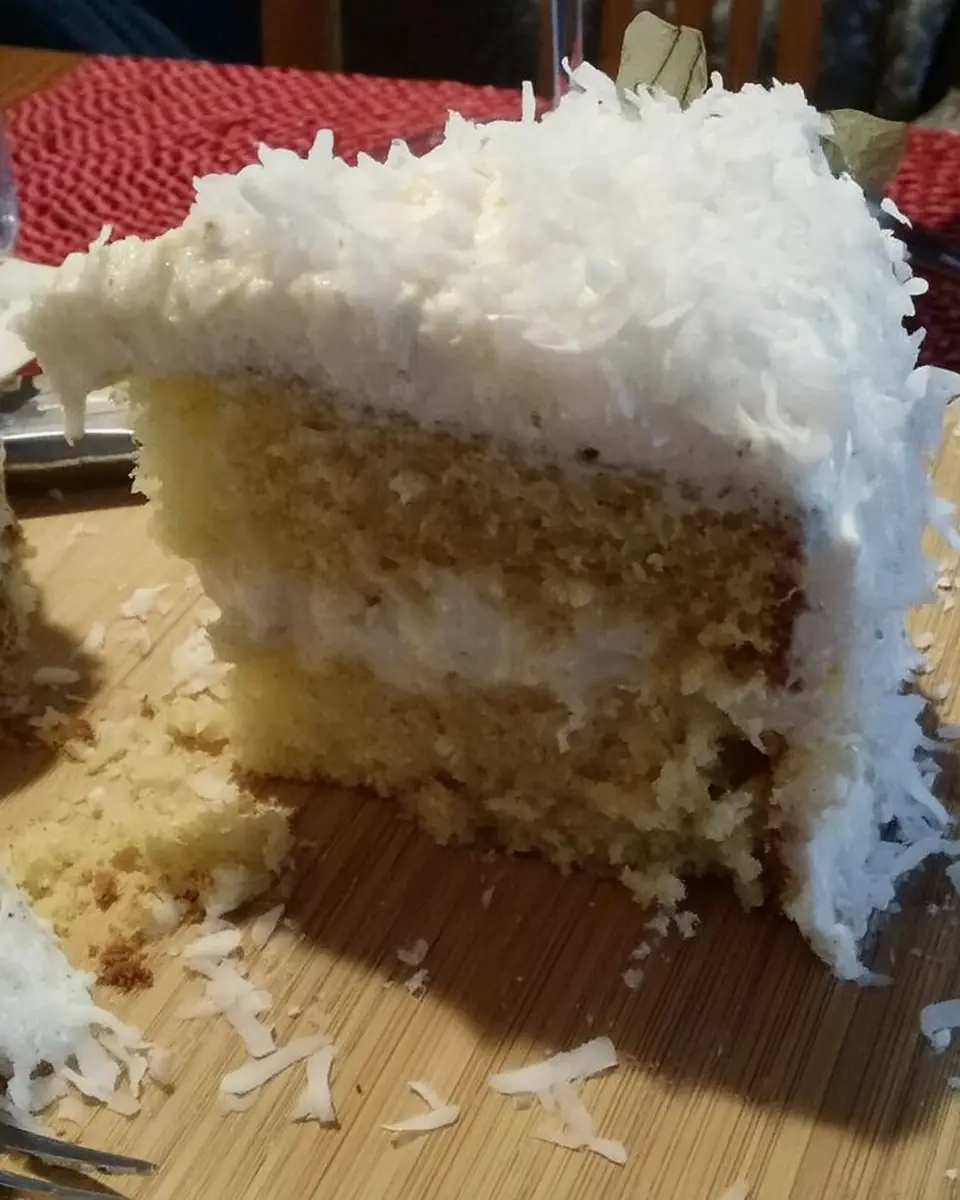 A thick, fluffy slice of homemade coconut cloud cake with three layers of moist yellow cake and creamy coconut frosting, topped with shredded coconut.