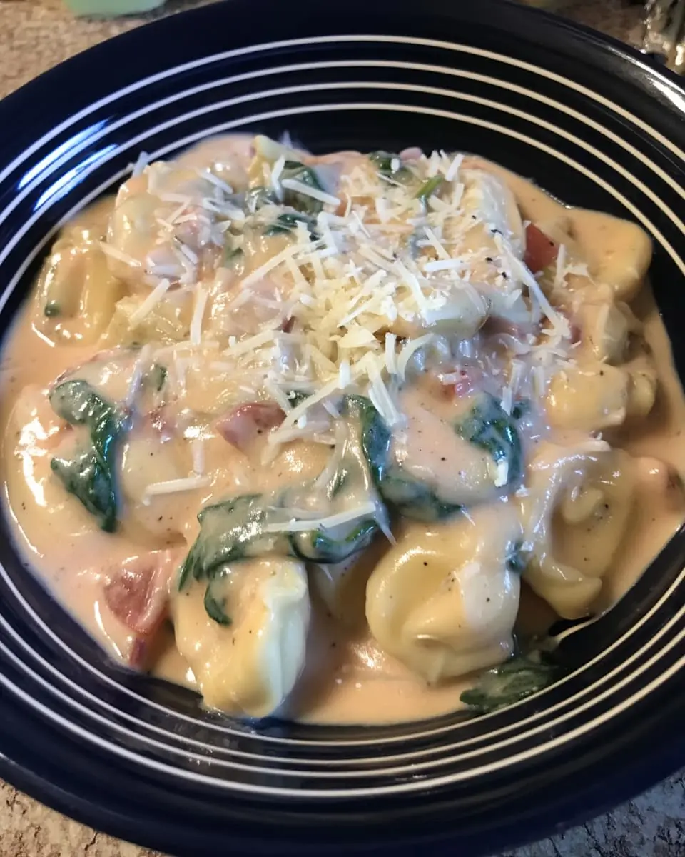 Bowl of creamy cheese tortellini tossed with baby spinach, diced tomatoes, and a sprinkle of grated Parmesan.