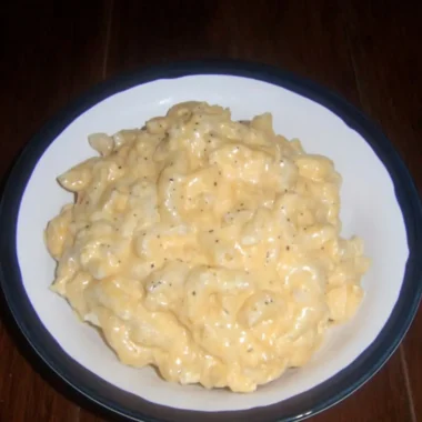 Bowl of creamy microwave mac and cheese, elbow pasta coated in rich cheddar sauce, on a dark wooden table