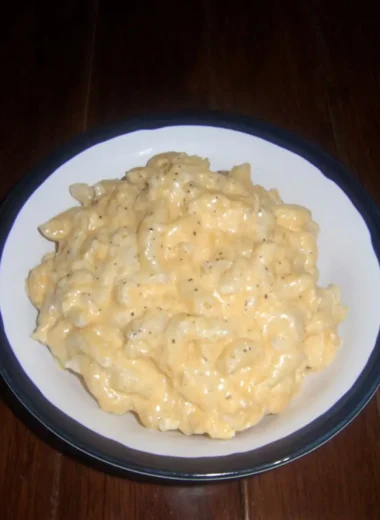 Bowl of creamy microwave mac and cheese, elbow pasta coated in rich cheddar sauce, on a dark wooden table