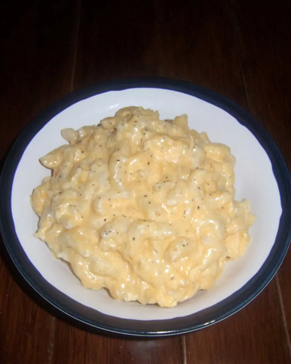 Bowl of creamy microwave mac and cheese, elbow pasta coated in rich cheddar sauce, on a dark wooden table