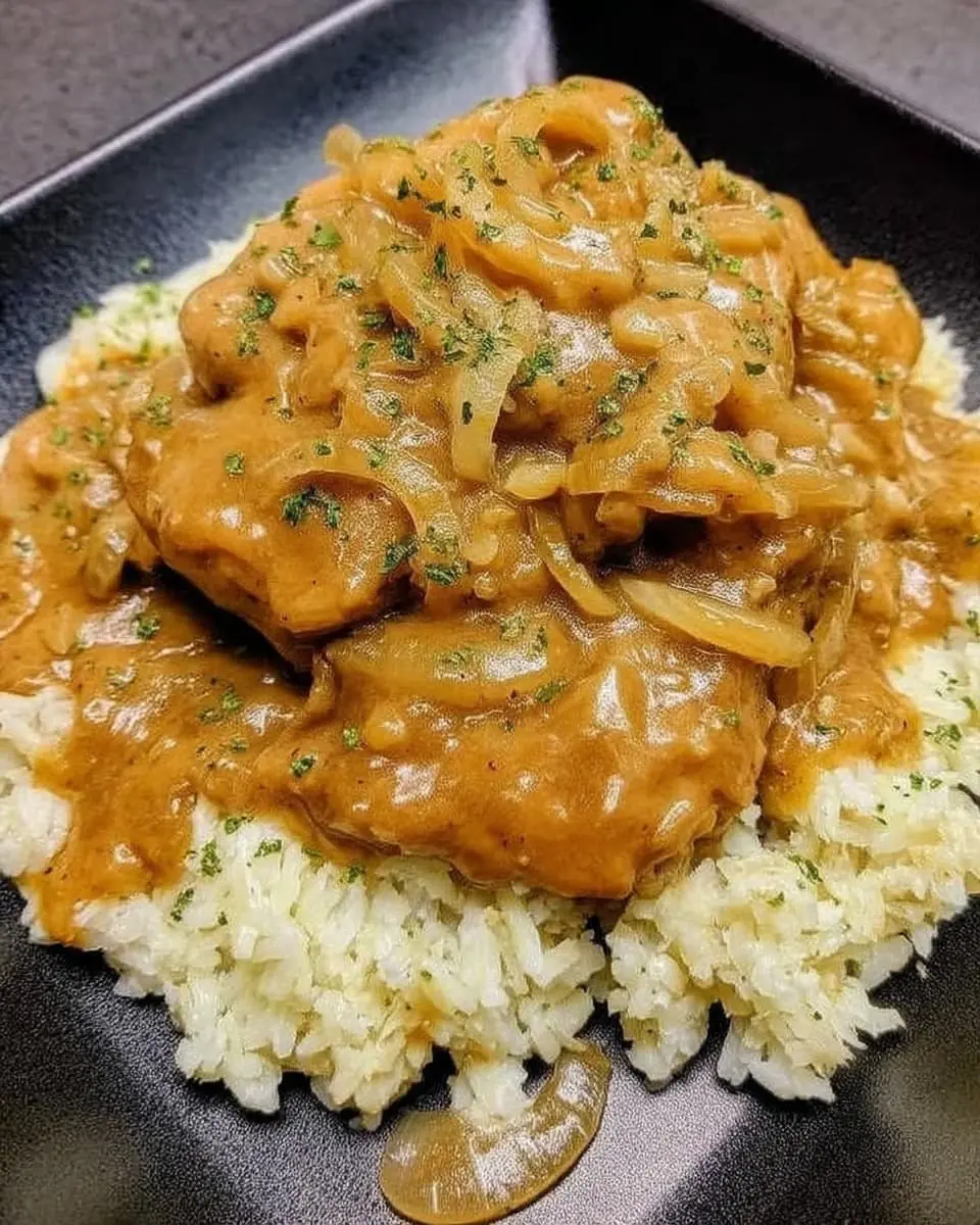Creamy smothered chicken and rice—pan-seared chicken cutlets blanketed in rich onion gravy, piled high on fluffy white rice.