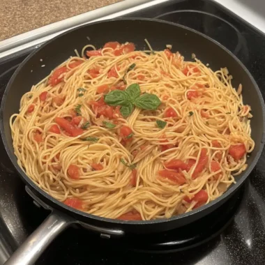 Spaghetti in a creamy fresh-tomato sauce topped with basil, cooking in a black skillet.