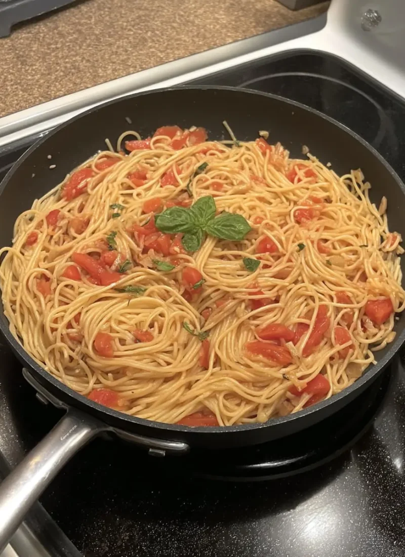 Spaghetti in a creamy fresh-tomato sauce topped with basil, cooking in a black skillet.