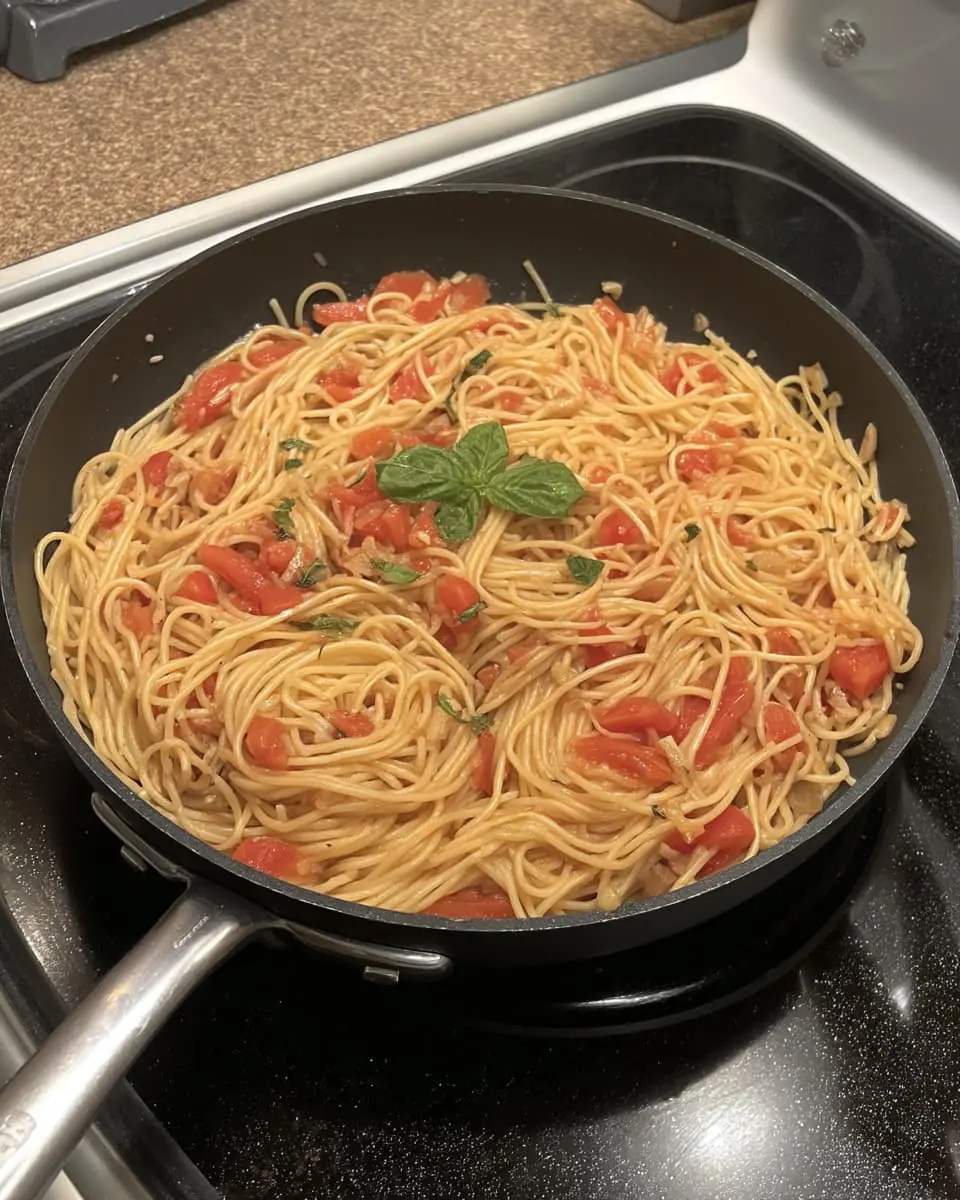 Spaghetti in a creamy fresh-tomato sauce topped with basil, cooking in a black skillet.