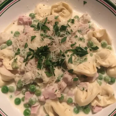 Creamy tortellini carbonara with diced ham, green peas, and fresh parsley in a shallow bowl.