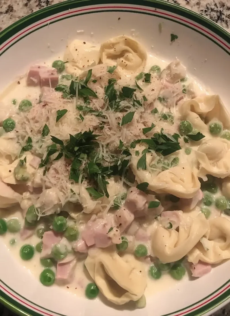Creamy tortellini carbonara with diced ham, green peas, and fresh parsley in a shallow bowl.