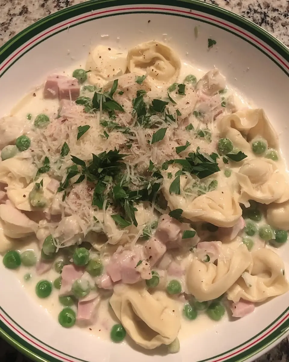 Creamy tortellini carbonara with diced ham, green peas, and fresh parsley in a shallow bowl.