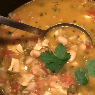 Creamy white chicken chili in a Dutch oven with chunks of chicken, cannellini beans, green chiles, tomatoes, and fresh cilantro garnish.