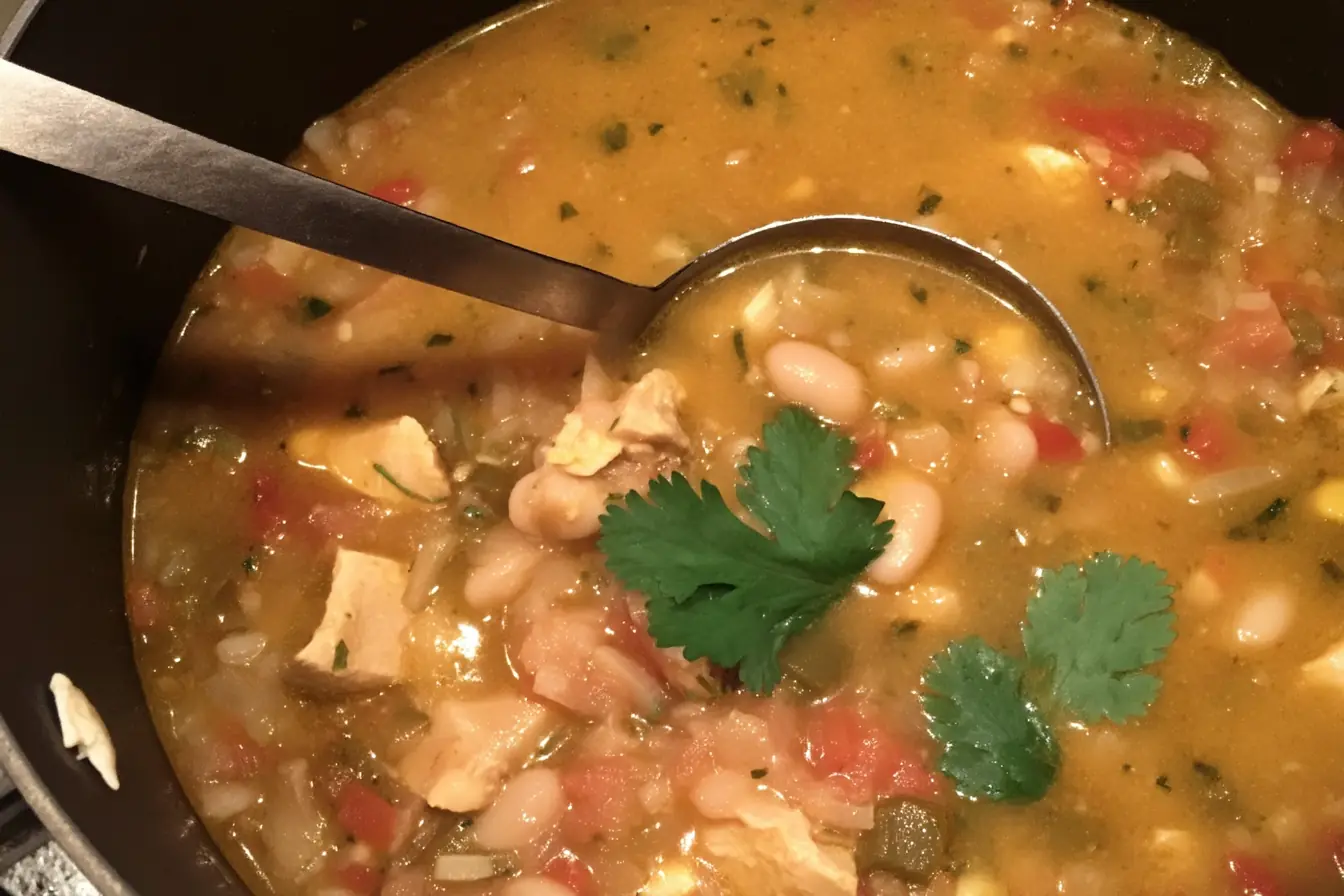 Creamy white chicken chili in a Dutch oven with chunks of chicken, cannellini beans, green chiles, tomatoes, and fresh cilantro garnish.