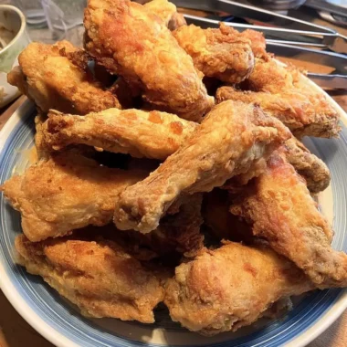 Golden-brown, extra-crispy chicken wings baked in the oven, stacked high on a blue-rimmed plate.
