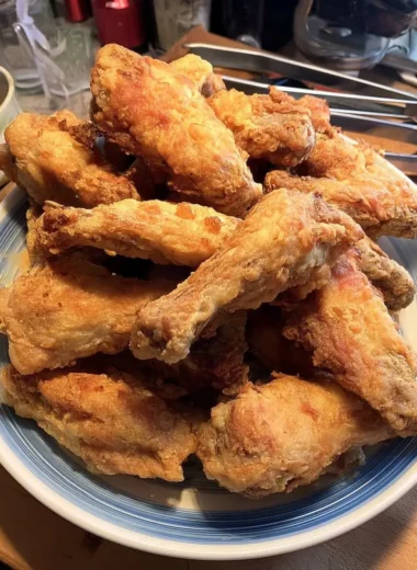 Golden-brown, extra-crispy chicken wings baked in the oven, stacked high on a blue-rimmed plate.