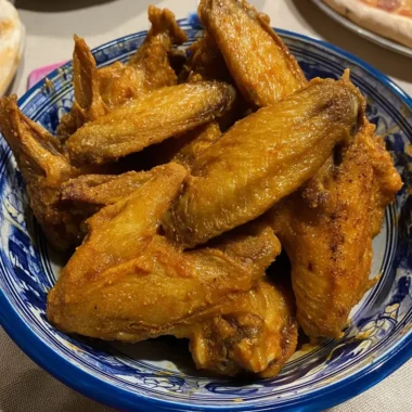 Crispy buffalo wings stacked in a blue ceramic bowl — an easy oven-baked chicken wing recipe.