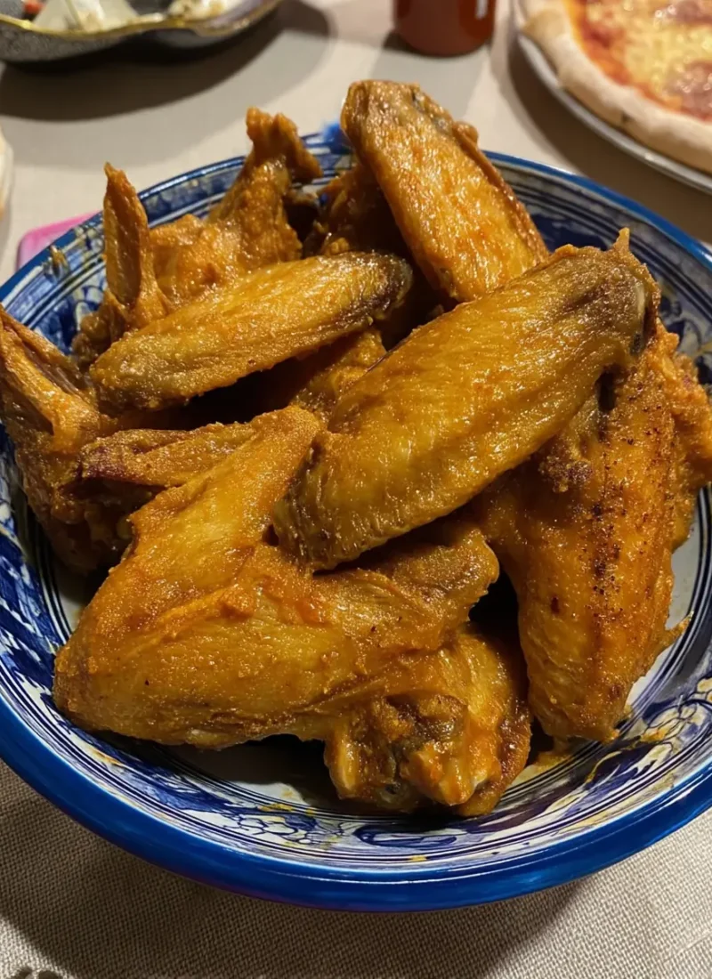 Crispy buffalo wings stacked in a blue ceramic bowl — an easy oven-baked chicken wing recipe.