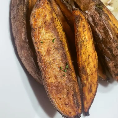 Close-up of golden, crispy potato wedges coated in spices and herbs on a white plate.
